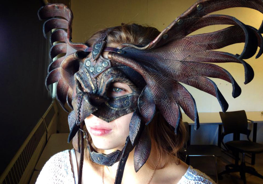 A woman in a leather half-mask that is modeled on the wingspan and beak of a raptor
