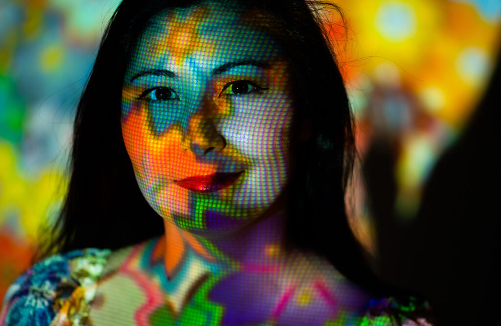 Closeup of Azsha White's face overlaid with a projection of bright, floral images.