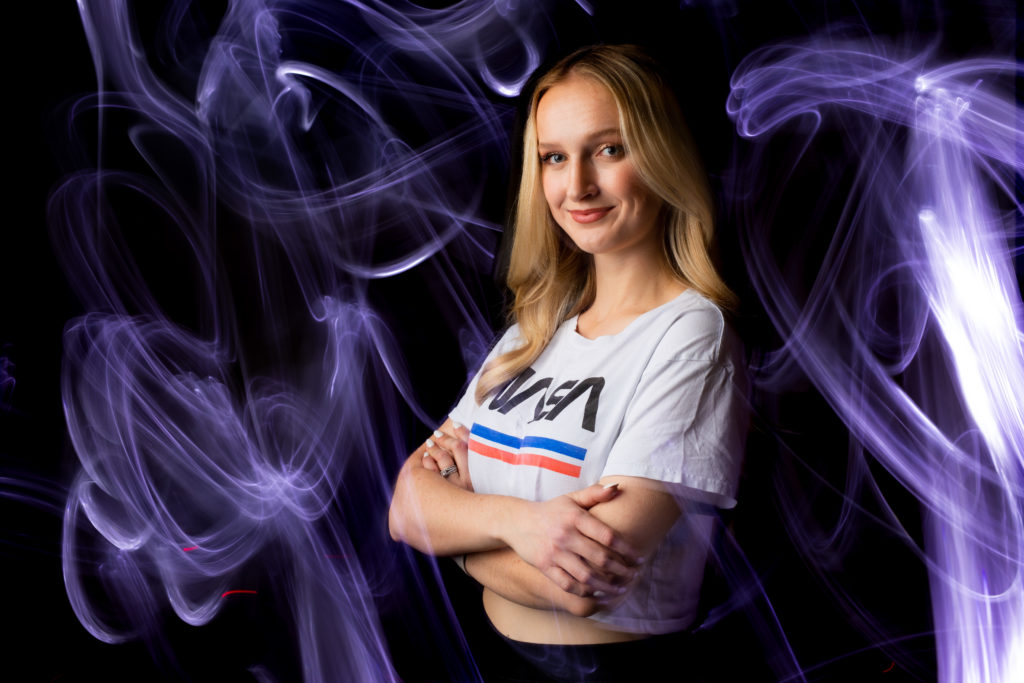 A portrait of Camille Calibeo, aka Galactic Gal, in the OCM studio with a NASA t-shirt photographed with a light painting technique