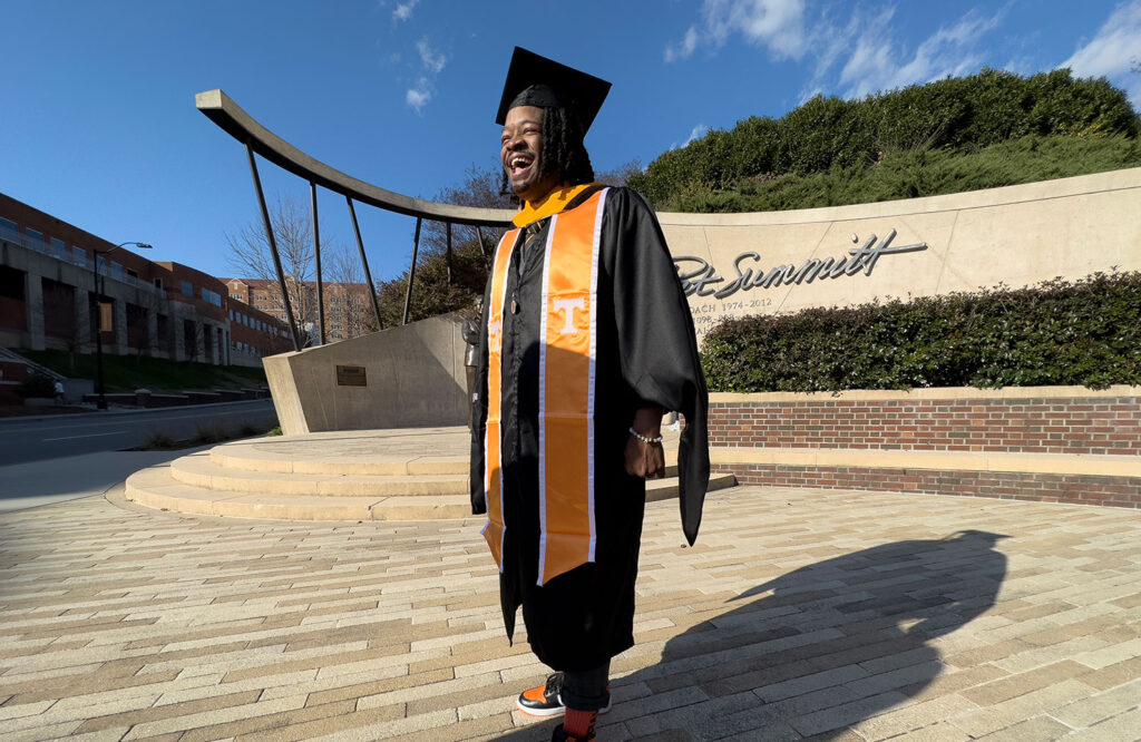 Charles Lowe stands in Pat Summitt Plaza wearing his commencement robes and orange Masters' sash