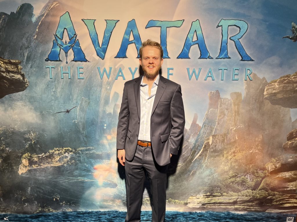 A man stands in front of a backdrop with a scene from a movie and the words Avatar: The Way of Water