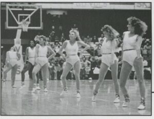 A group of women dancing in white leotards on a basketball court