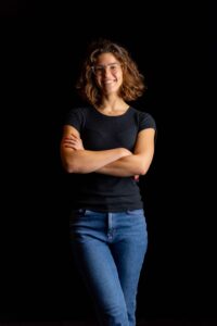 Woman standing against a black background wearing a black T-shirt and jeans