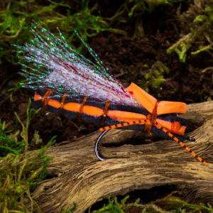 Orange and black fishing lure with iridescent white fibers and red beads for eyes, designed to look like a Brood X cicada, resting on a log.