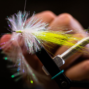 A close-up photograph of a yellow and white hand-tied fly used as a lure to catch trout.