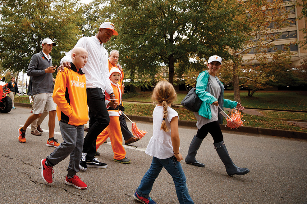 Josh Dobbs walks through campus while interacting with several orange clad children
