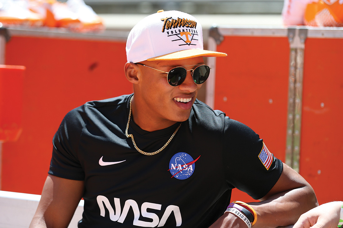 Josh Dobbs sits at the orange and white game wearing a black NASA shirt and a white Tennessee ball cap