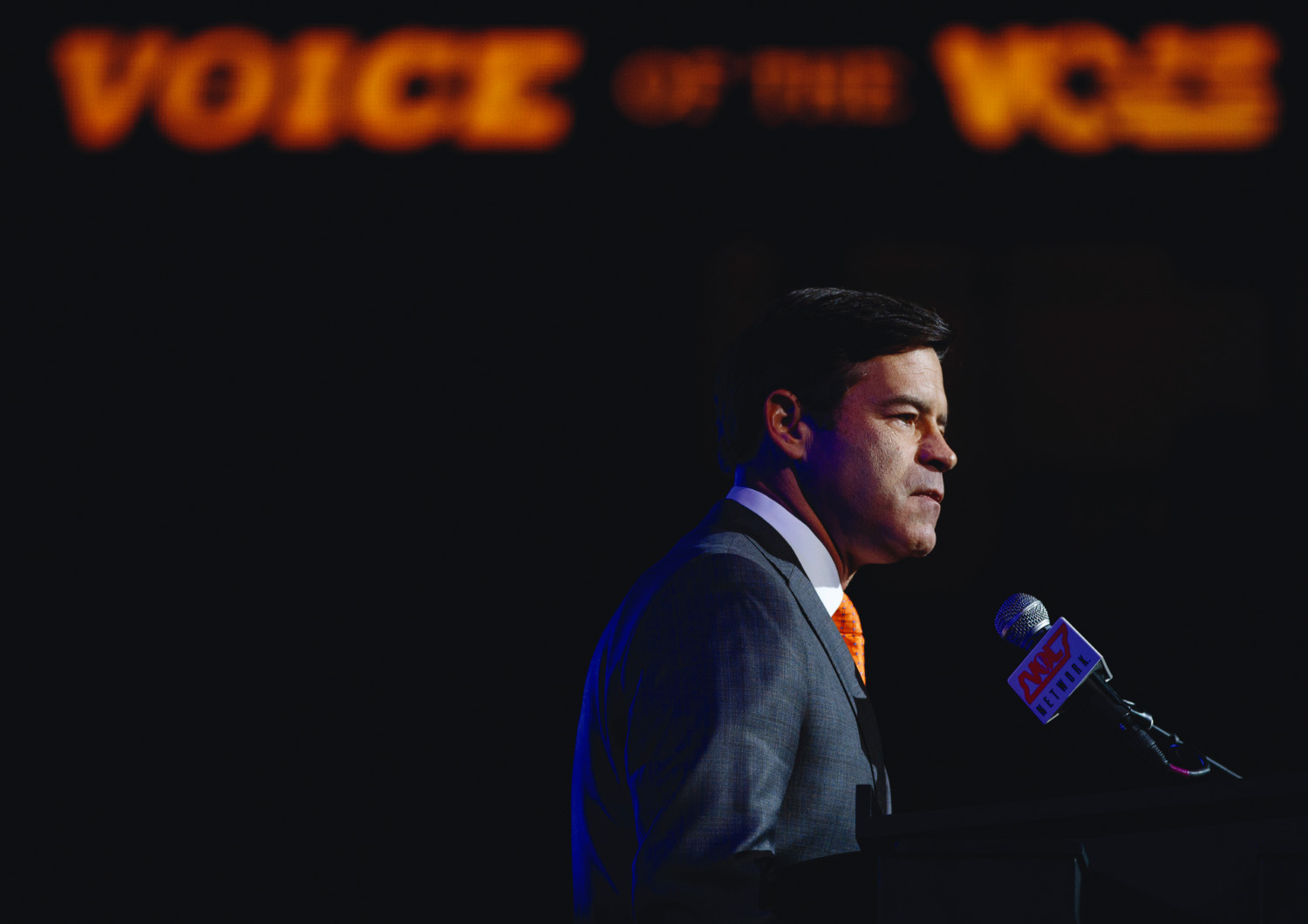 voice-keith_side Mike Keith is photographed from the side against a dark background speaking into a microphone, the words Voice of the Vols above his head