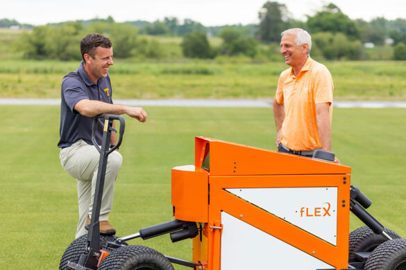 Kyley Dickson and John Sorochan stand behind the fLEX machine, which has an orange and white boxlike body from which four big wheels are extended by shock absorbers