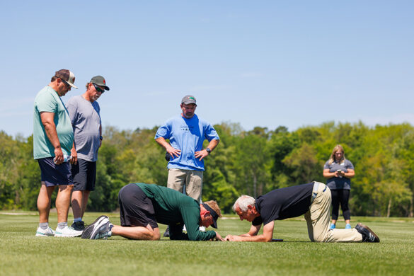 Keith Salmon and John Sorochan kneel down close to the turfgrass, supported by their elbows with their heads facing one another, examining the growing grass.